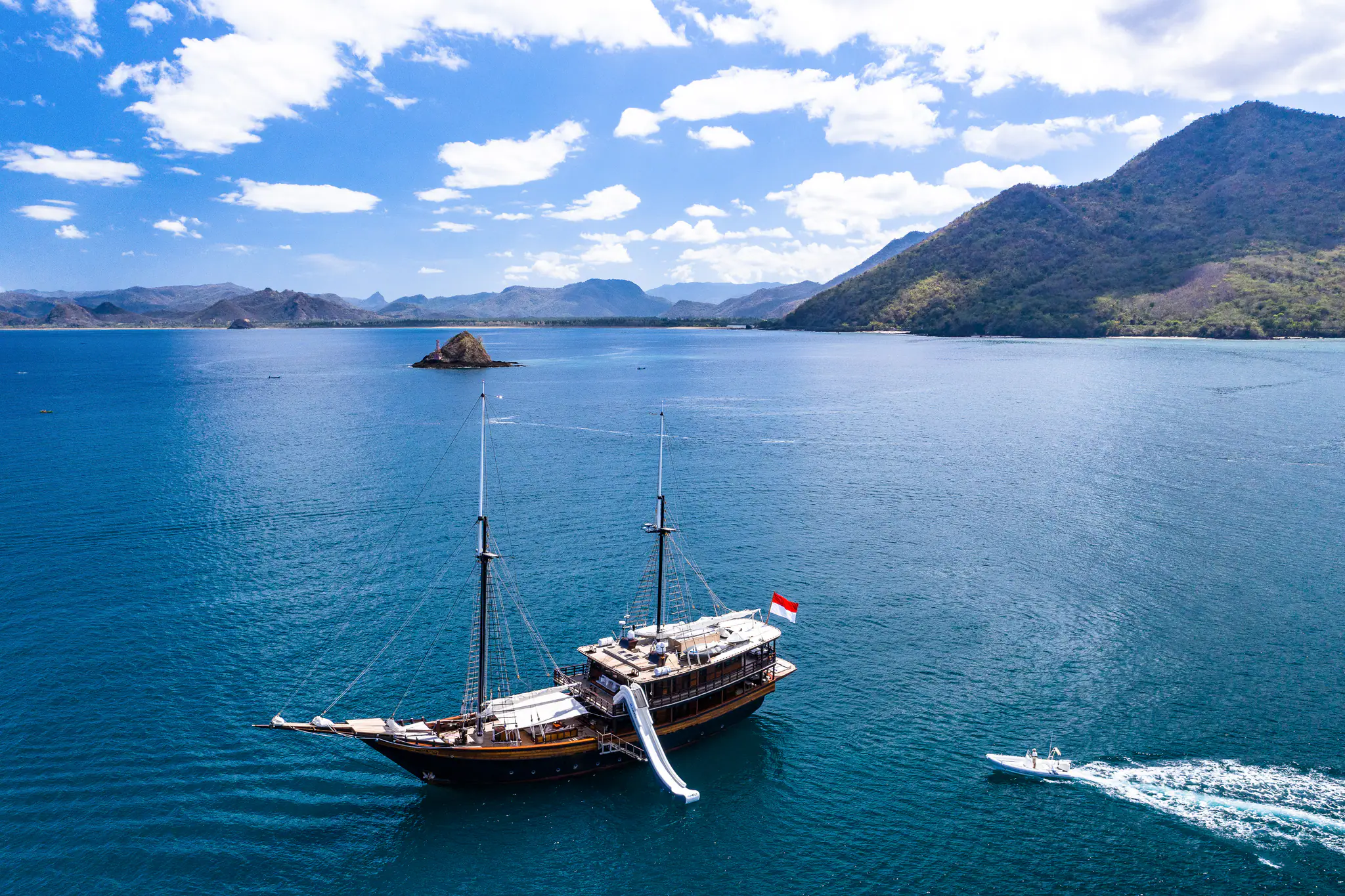 Dunia Baru at anchor in a wide Komodo bay, her inflatable water slide down to the sea and a tender heading out