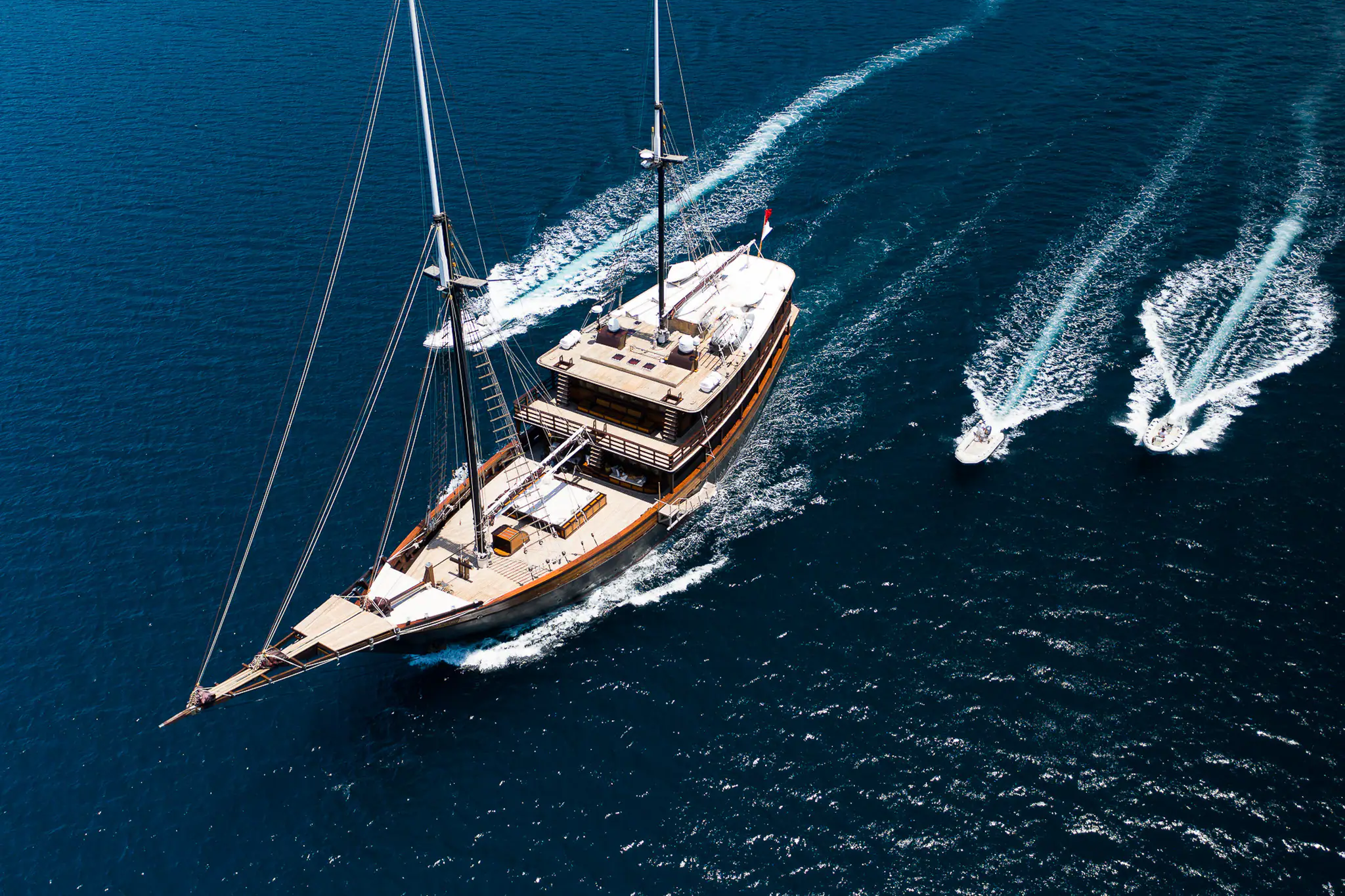 Dunia Baru from above, underway with her two tenders racing alongside in deep blue water