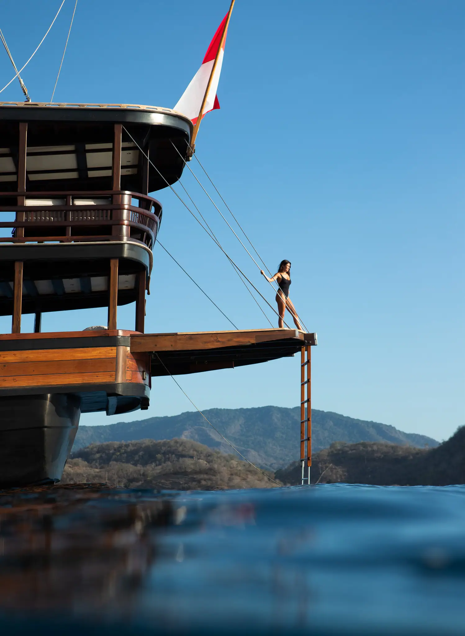 A guest on Dunia Baru's lowered stern platform, stepping off into clear water under the aft deck