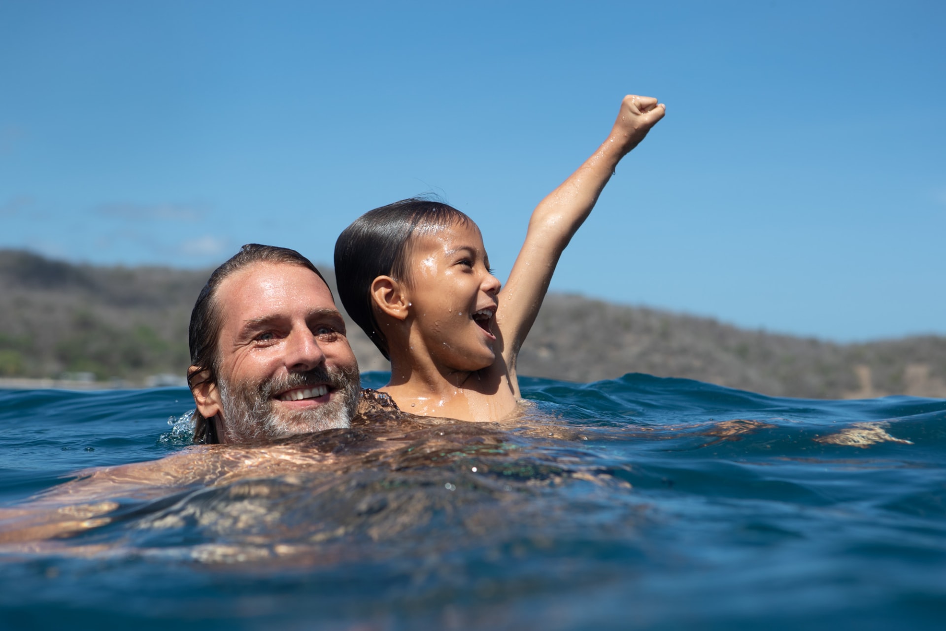 A father and son swimming in the sea off Dunia Baru, the boy punching the air