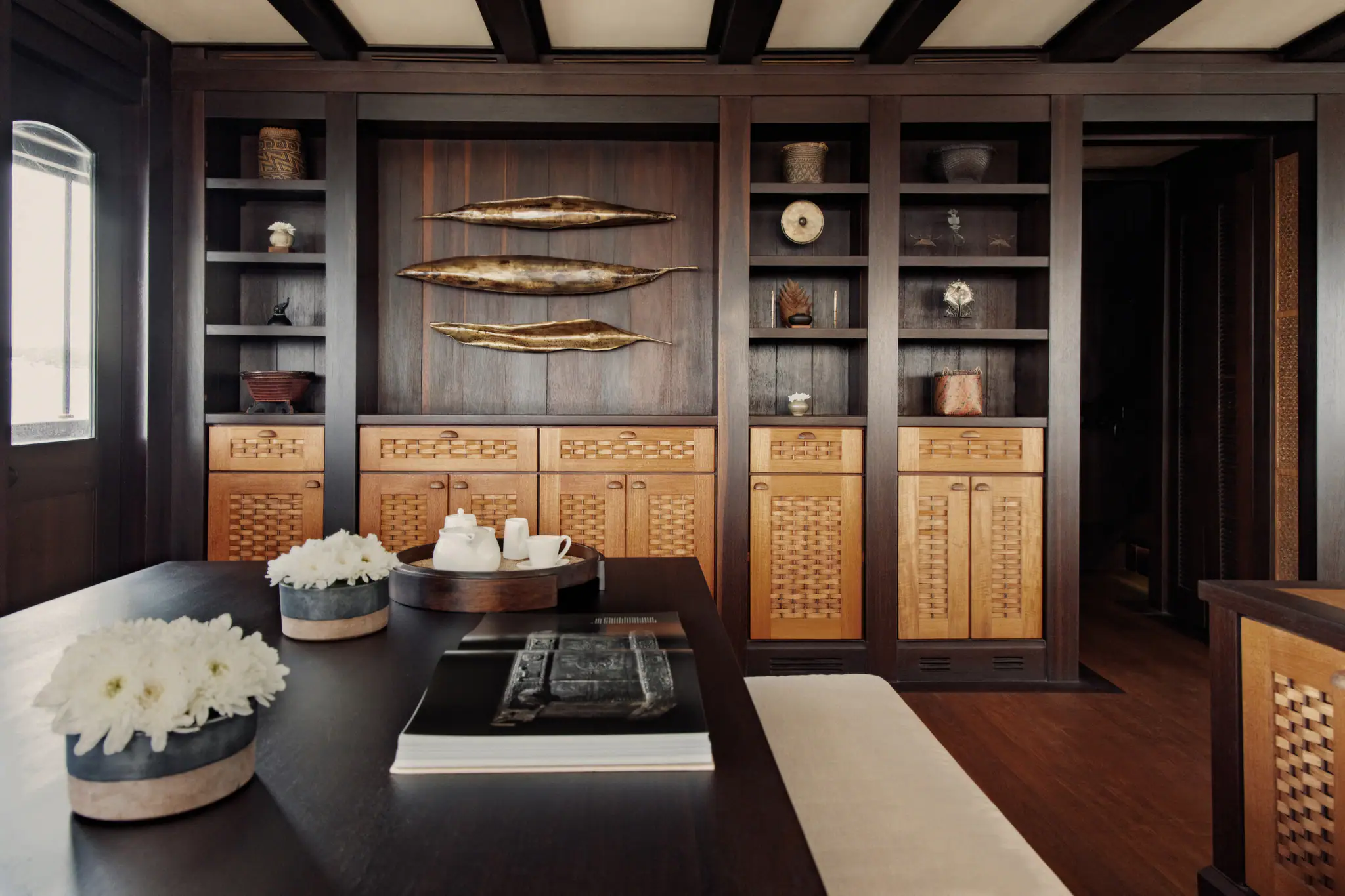 Dunia Baru's saloon: dark timber shelving, carved panels and a reading table set with white orchids