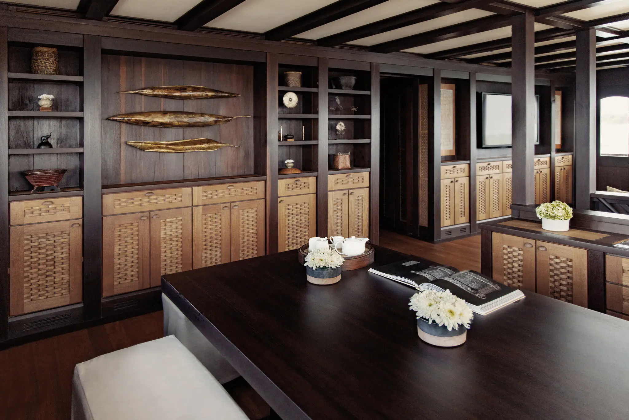 The panelled saloon aboard Dunia Baru, with woven cabinetry, a long dark table and brass details