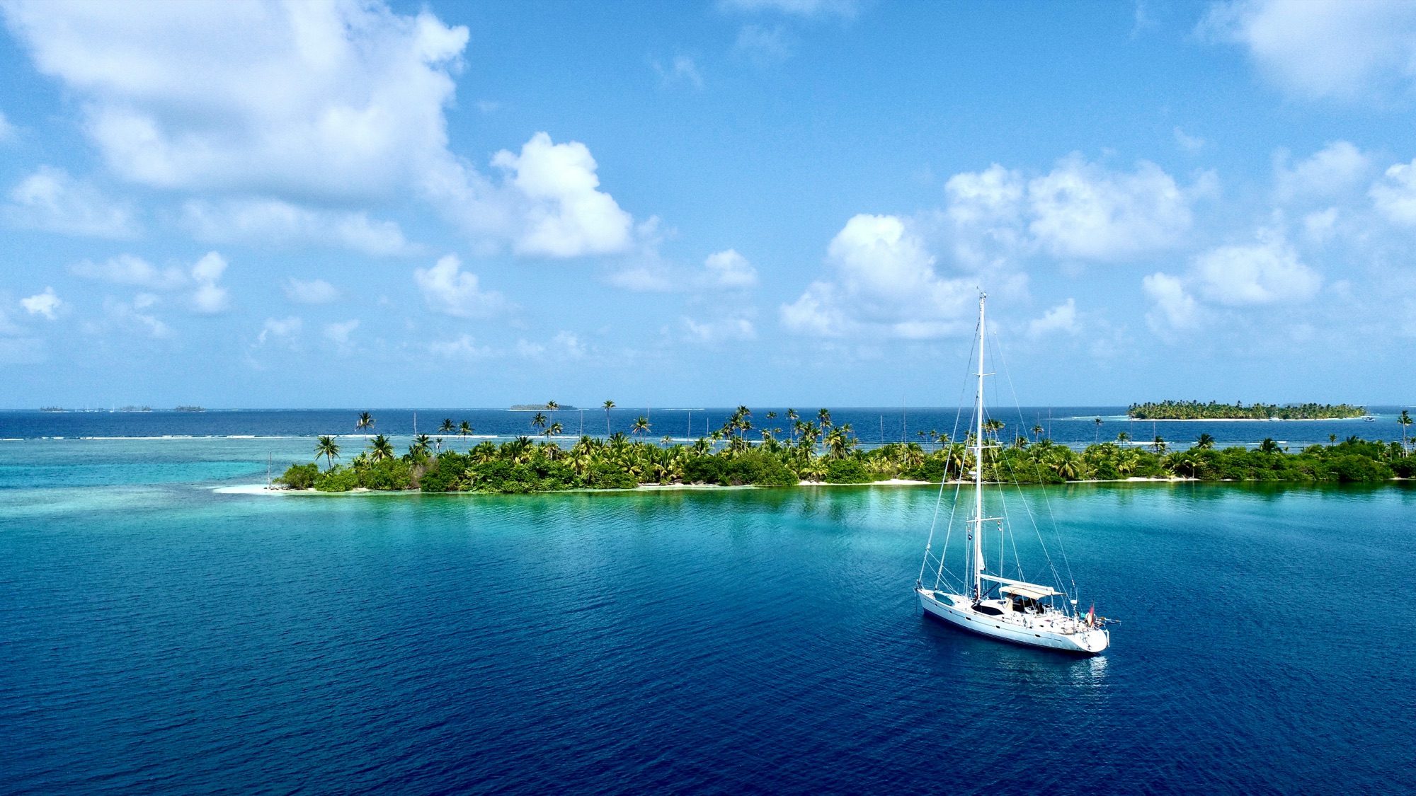 A sailing yacht at anchor inside a palm-fringed atoll