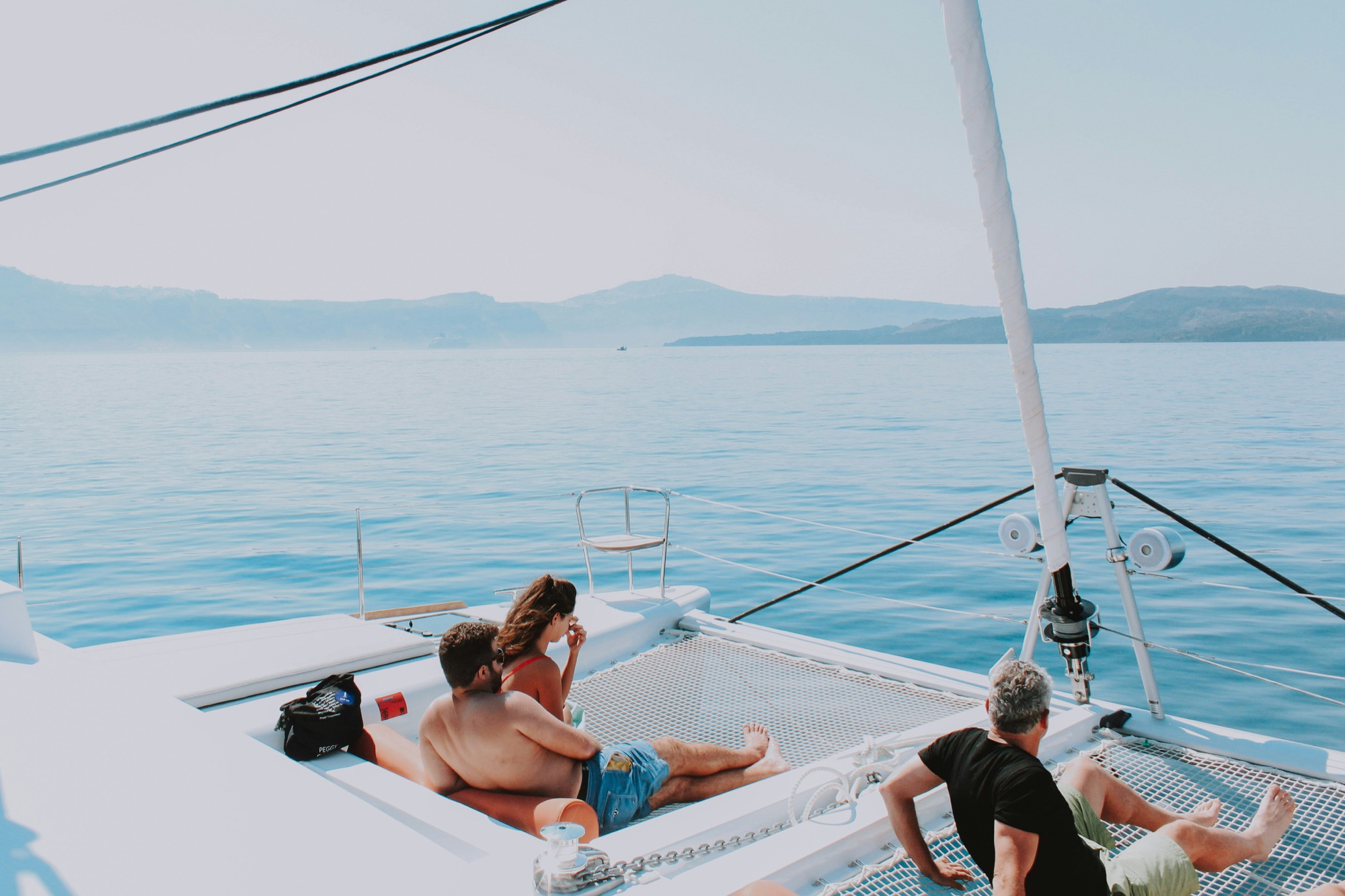 Guests on the foredeck of a catamaran at anchor, mountains beyond the water
