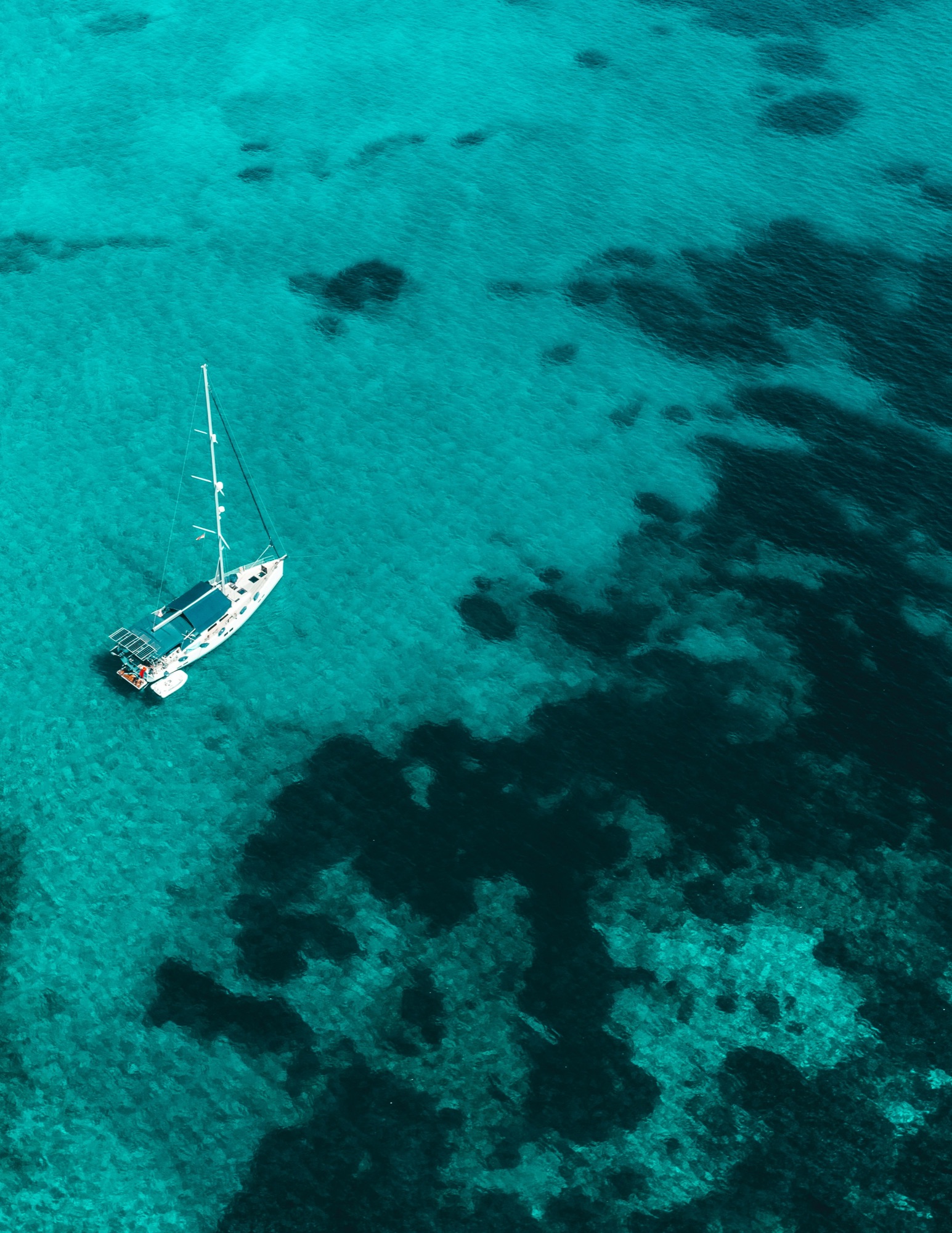 Aerial view of a yacht anchored over turquoise reef
